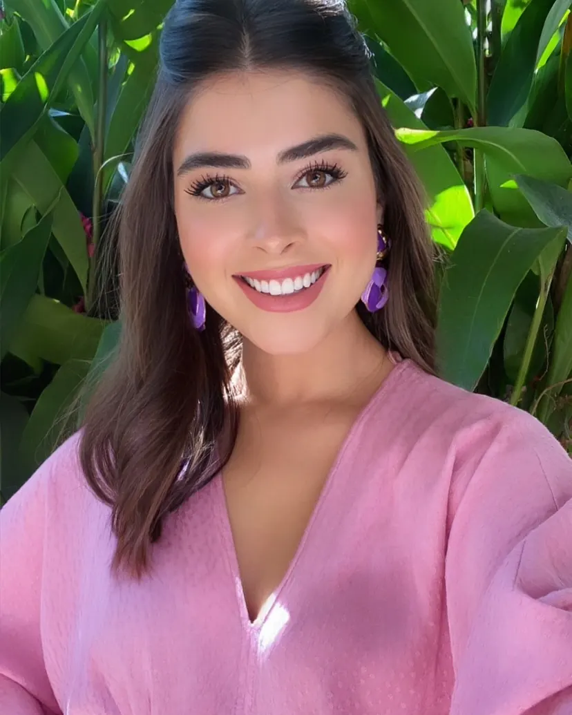 Stephanie sorrindo, de blusa rosa, com folhagens ao fundo